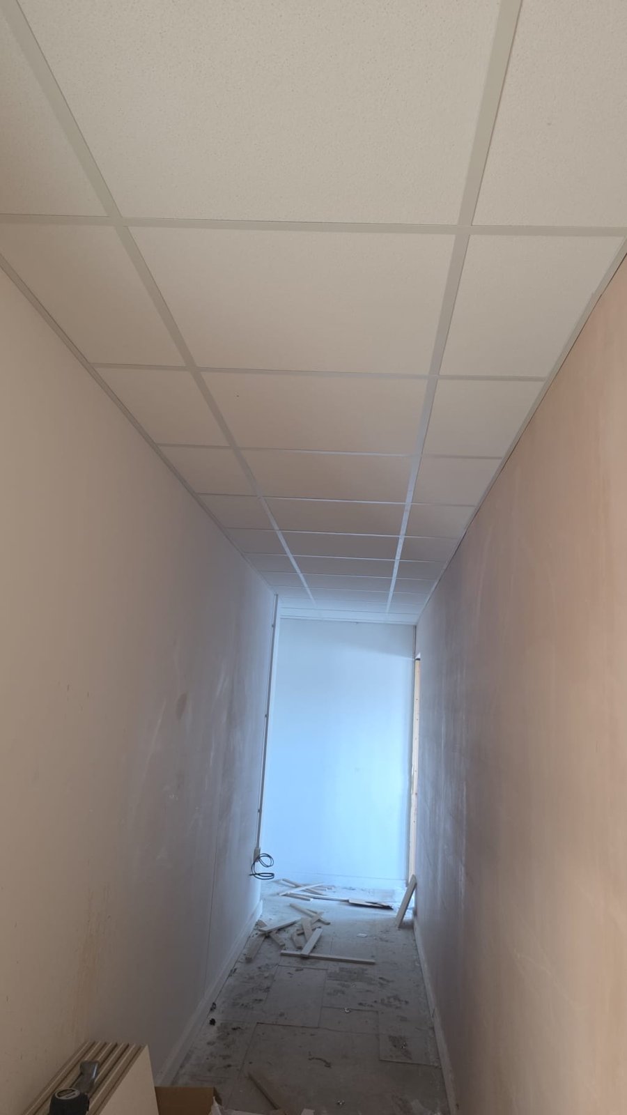 Grid ceiling installation along a boarded corridor